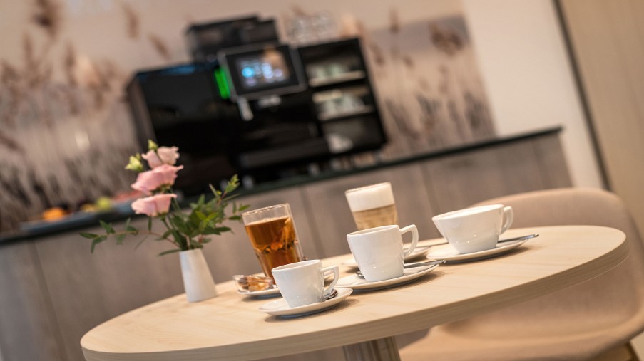 Im Vordergrund Kaffetassen. Im Hintergrund Kaffeautomat